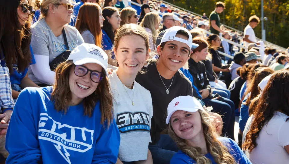 A group of UNE students poses for a photo in the stands at Homecoming