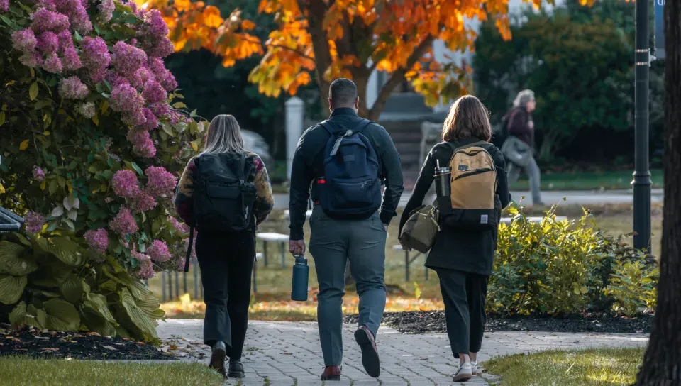 Three students walk across the Portland Campus quad during autumn